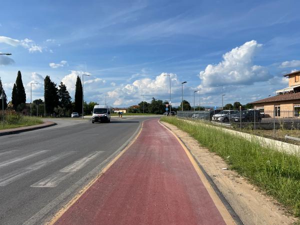 Route pavée dans une zone semi-urbaine. À droite, piste cyclable rouge parallèle à la route principale